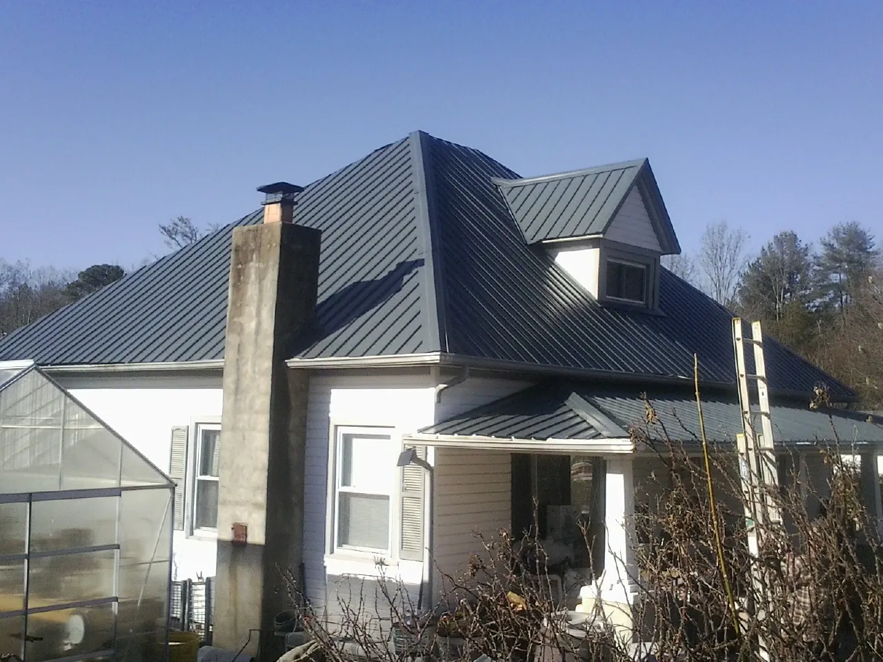 Dark blue standing seam metal roof on a white farmhouse with dormer — Slate & Tile Roof Repair by Roofing Brothers in Wymore