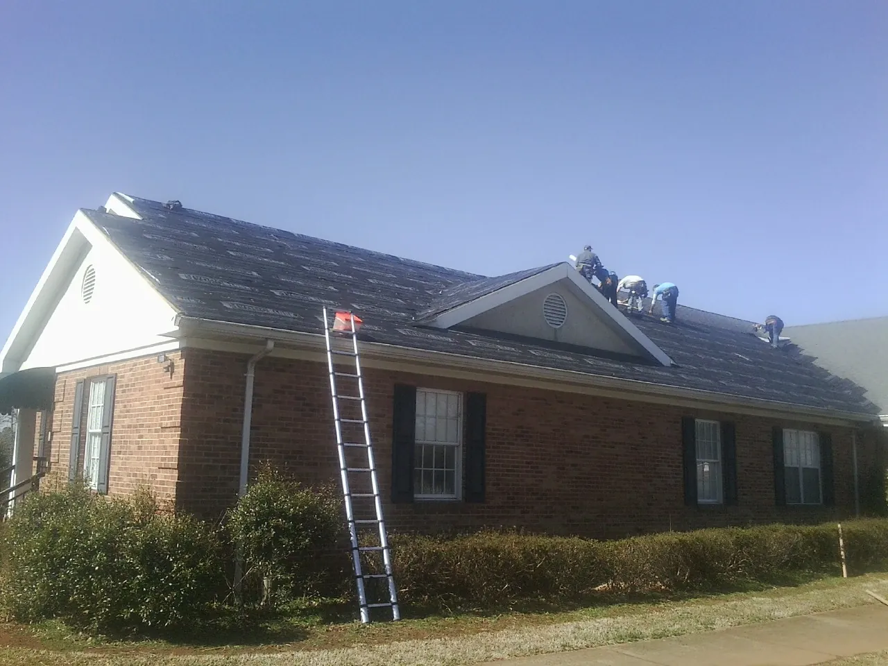 Crew tearing shingles off a brick ranch roof with a ladder set — Emergency Roof Repair work by our crew in Wymore