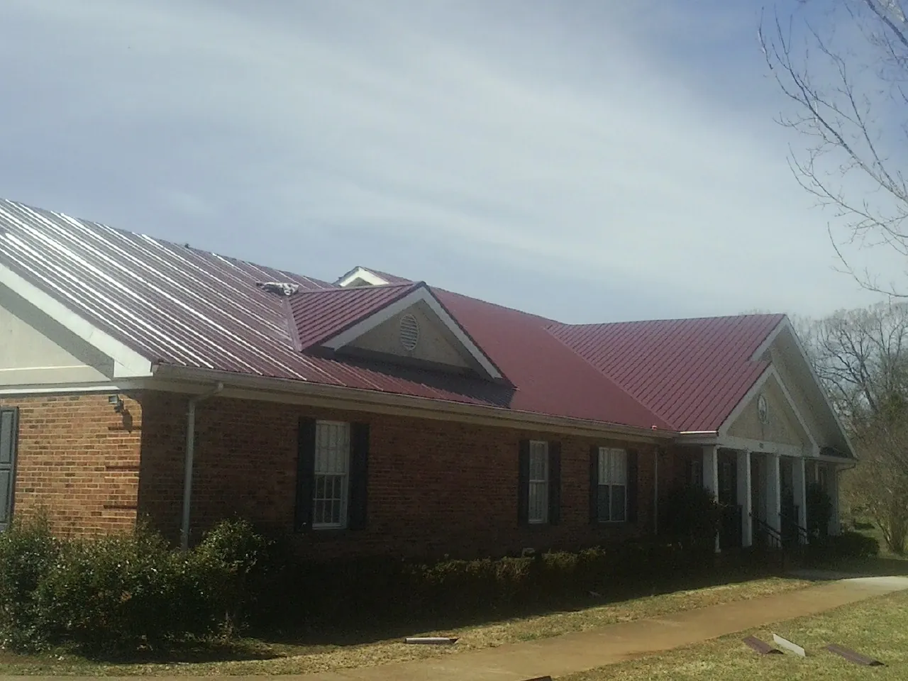 Red metal roof with gabled entries on a long brick building, from a Hail Damage Roof Repair job in Wymore
