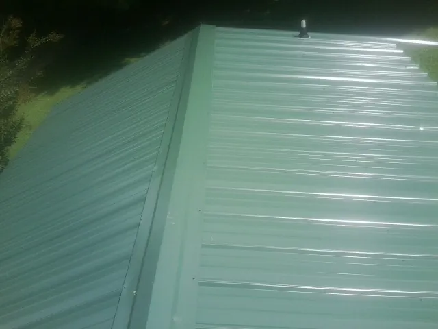 New green metal panels meeting at the ridge of a roof — Flat Roof Repair work by our crew in Wymore