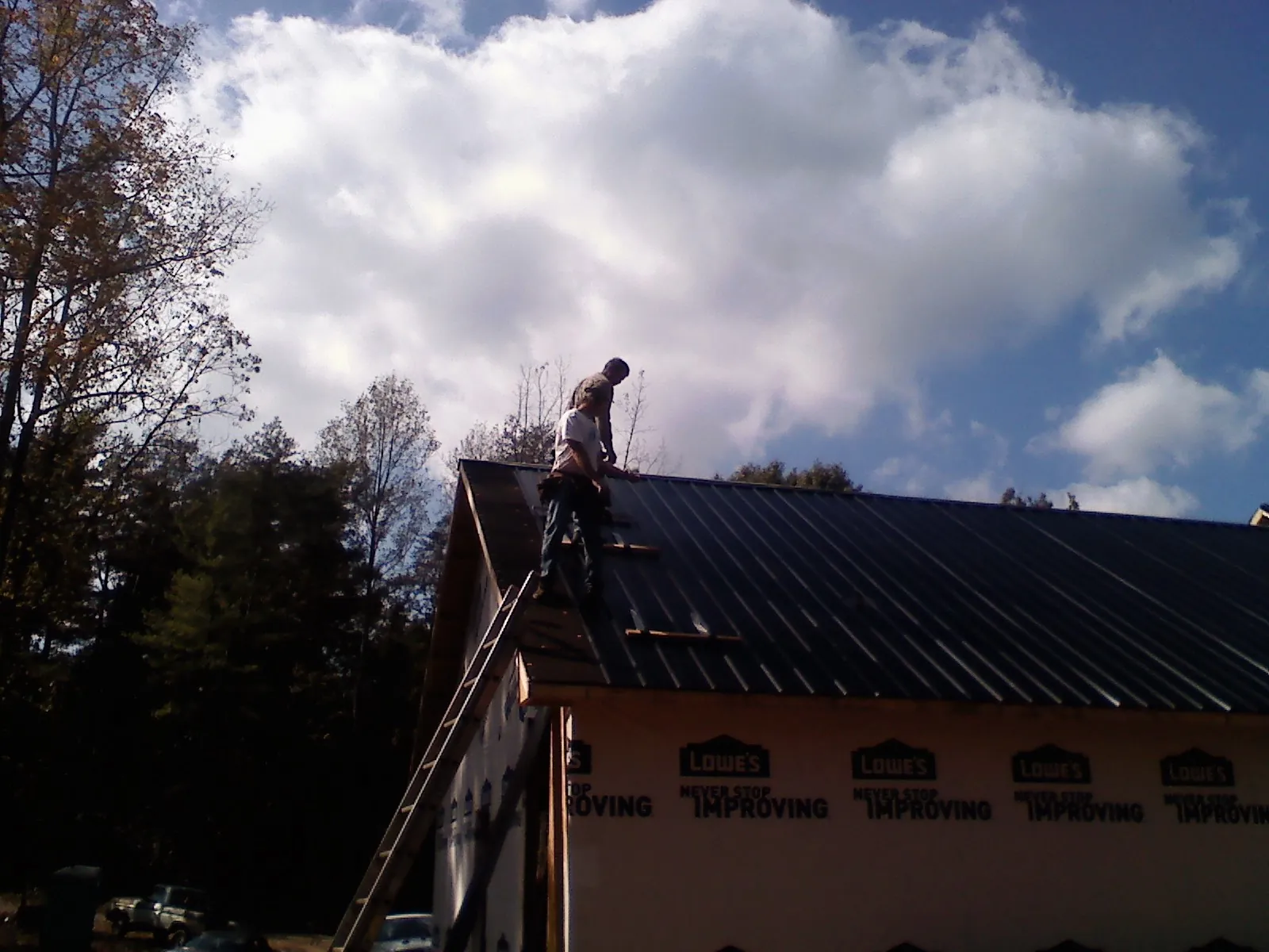 Roofer fastening dark metal panels high against a cloudy sky, from a Roof Inspection job in Wymore