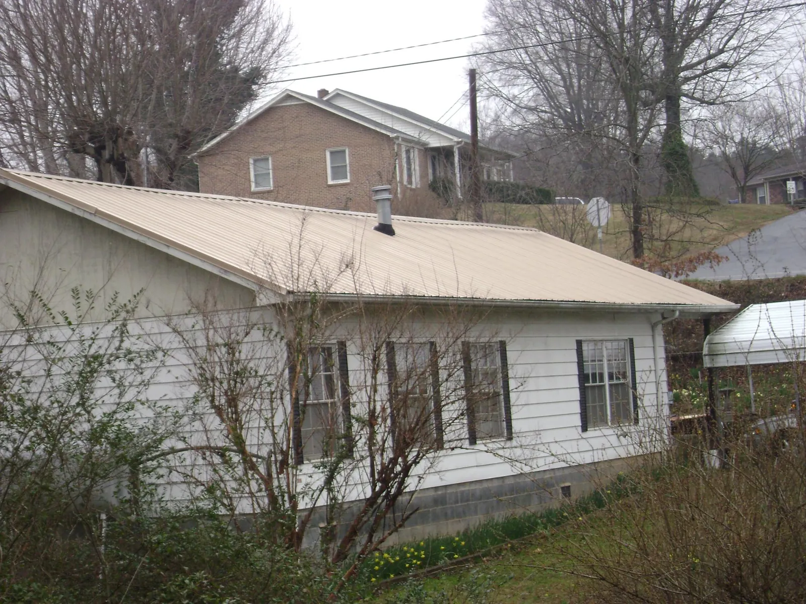 Tan metal roof on a white sided house set into a hillside — Commercial Roofing by Roofing Brothers in Wymore
